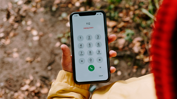 Henkilö pitää kädessään puhelinta, jossa on esillä hätäpuhelun numeronäppäimistö. Puhelimen näytöllä lukee "112 Hätäpuhelu".