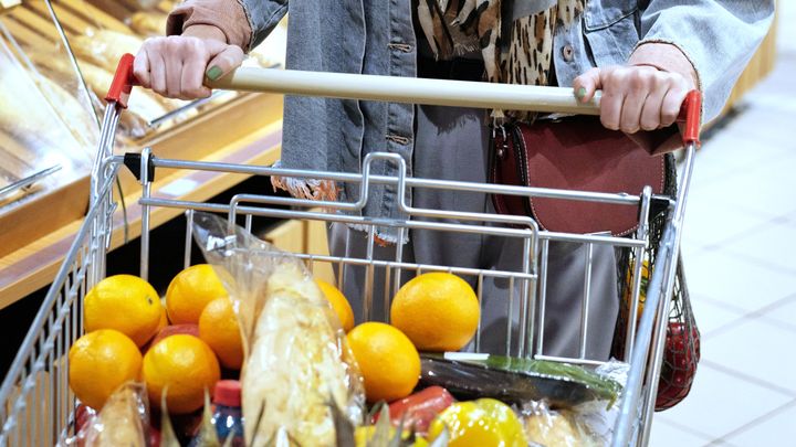 En person i dagligvaruhandeln skjuter kundvagnar med frukt, bröd och andra dagligvaror.