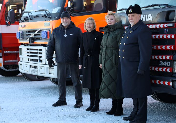 Neljä ihmistä seisoo paloautojen edessä