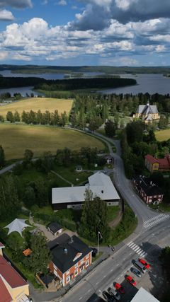 Ilmakuva maalaismaisemasta, jossa näkyy Vinhan kirjakauppa, kirkko sekä järvi taustalla.