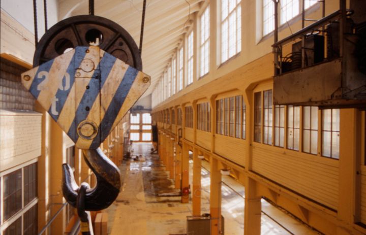 Vanhan teollisuushallin sisätila, jossa on suuria ikkunoita ja suuri metallinen nostokoukku katossa.