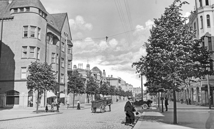 Mustavalkoinen valokuva Hämeenkadun ja Kuninkaankadun risteyksestä vuodelta 1913. Vasemmalla Blomin talo ja oikealla Pulla-Helinin talo. Katu kivetyksellä, hevoskärryt ja vanha auto näkyvät tiellä.