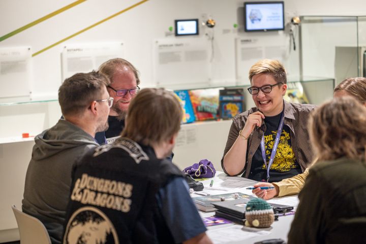Ryhmällinen ihmisiä istuu pöydän ääressä ja pelaa roolipeliä.