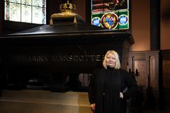 A woman stands next to a large historical sarcophagus with stained glass windows in the background.