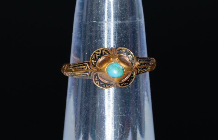 Alt text: Gold ring with black enamel and turquoise stone on display.