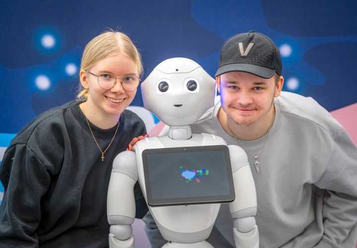 Kaksi henkilöä poseeraa robotin kanssa.