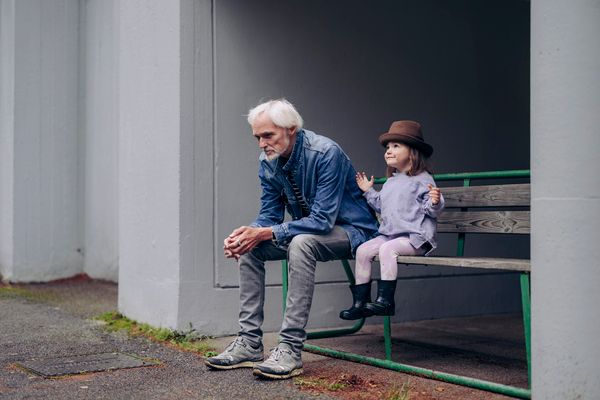 Mies istuu lapsenlapsensa kanssa kerrostalon edustalla olevalla penkillä.