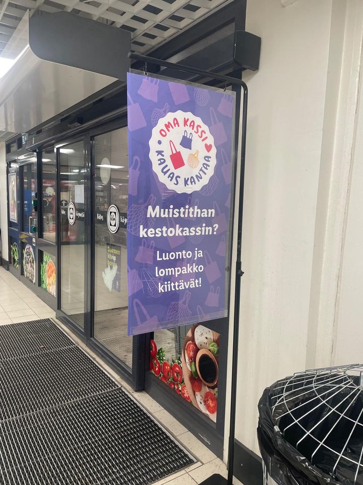 Lidl laittaa myymälöidensä edustalle kyltit muistuttamaan omasta kassista.