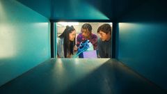 Kuva otettu laatikosta käsin. Suuaukolla kolme nuorta katsoo toisiaan ja pitelee käsissään sinistä lenkkaria.