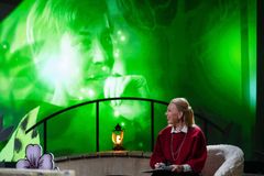 Nainen punaiseen pukeutuneena istuu sisätiloissa, taustalla näkyy muuta kuvaa.