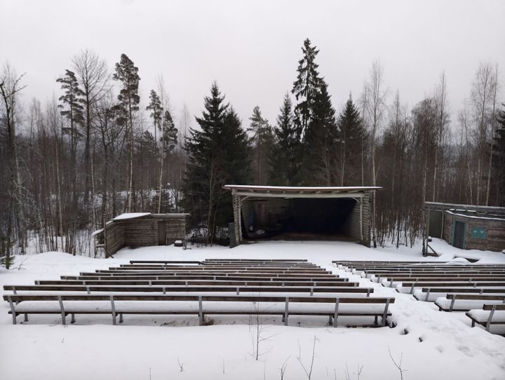 Lumisen maiseman keskellä on ulkoilmateatteri, jossa on puurakenteinen esiintymislava ja tyhjiä penkkirivejä.