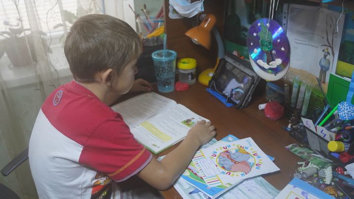 Poika tekee läksyjä pöydän ääressä, kirja edessään.