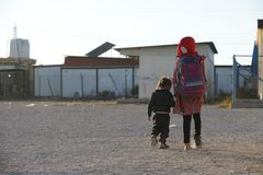 Lapset kulkevat selin ja käsikädessä pakolaisleirillä.