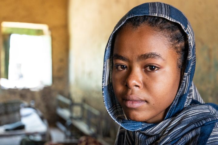 Nuori tyttö huivissa katsomassa kameraan sisätiloissa.