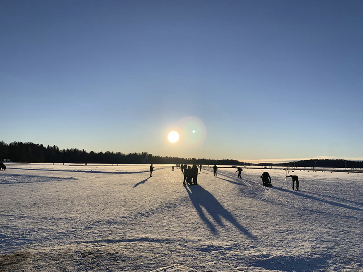 Aurinkoinen talvimaisema Aurlahden rannasta. Ihmisiä kävelee jäällä kaukana horisontissa.