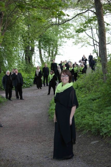 Paikallisia laulajia luonnon ympäröimänä, pukeutuneina mustiin asuihin ja vihreisiin huiveihin.