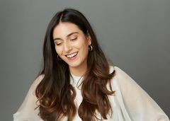 "Nuori nainen, pitkät tummat hiukset, hymyilee katse alaspäin."