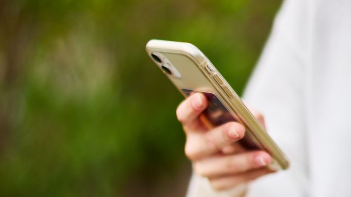 Henkilö pitää kädessään älypuhelinta vihreässä ympäristössä.