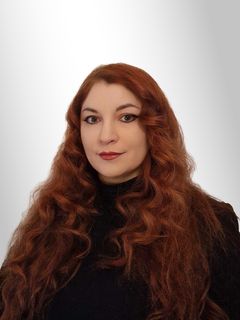 Väittelijän potrettikuva, nainen katsoo kohti kameraa,  naisella on pitkät punaiset kiharat hiukset ja yllään musta poolokauluksinen pusero