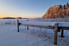 Talvinen Saimaa järvimaisema Savonlinnassa, aurinko laskee lumisen maiseman yllä, kuuraisia puita taustalla.