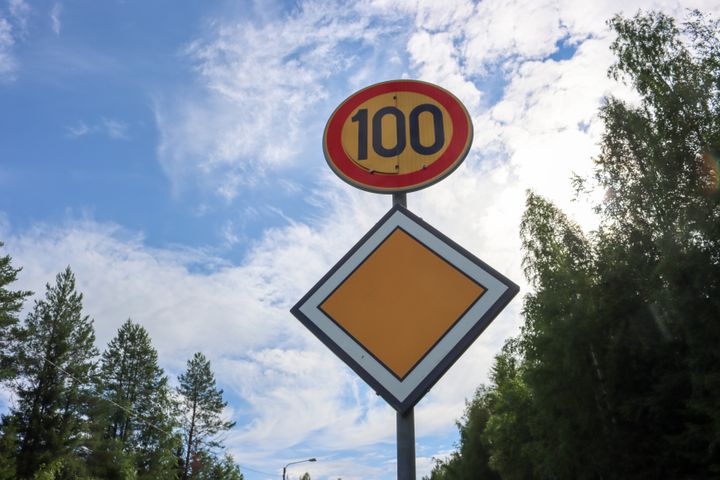 Liikennemerkki, joka näyttää nopeusrajoituksen 100 km/h. Taustalla on metsää ja sininen taivas pilvineen.