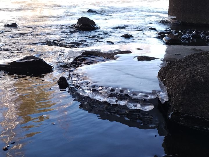 Vettä virtaa osittain jäisessä joessa.